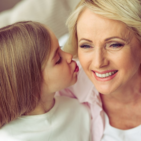 Dental Cleanings Ensuring Healthy Grins A happy woman and a little girl kissing a woman on the cheek