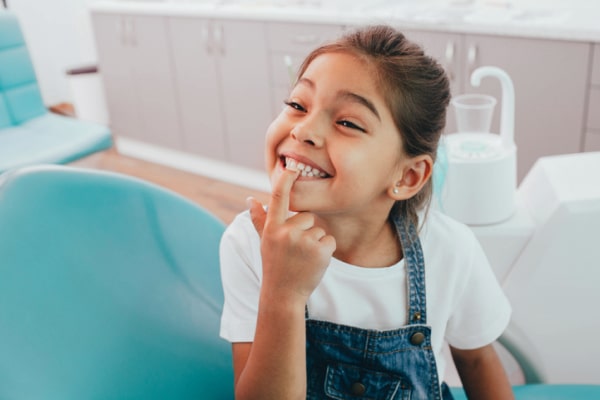 Emergency Dental Care A little girl at the dentist showing her teeth while pointing her finger at her mouth